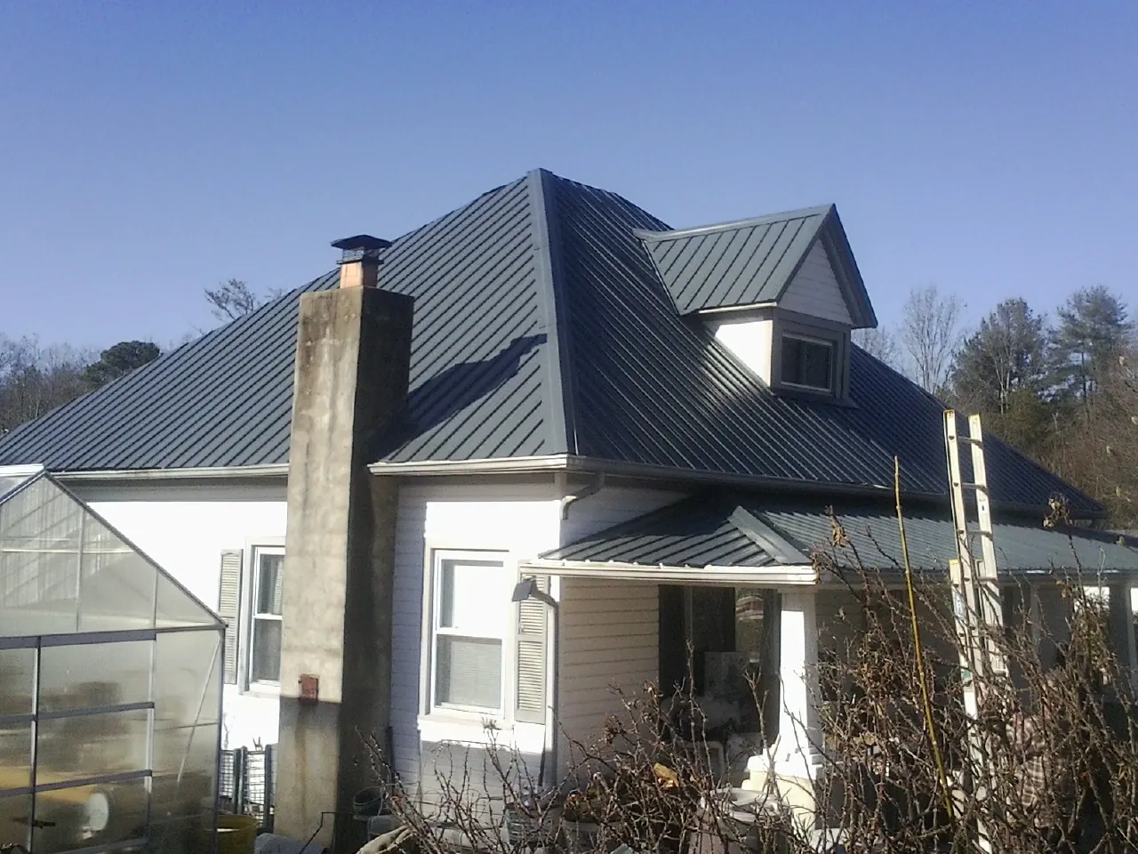 Dark blue standing seam metal roof on a white farmhouse with dormer — Slate & Tile Roof Repair by Roofing Brothers in Rio