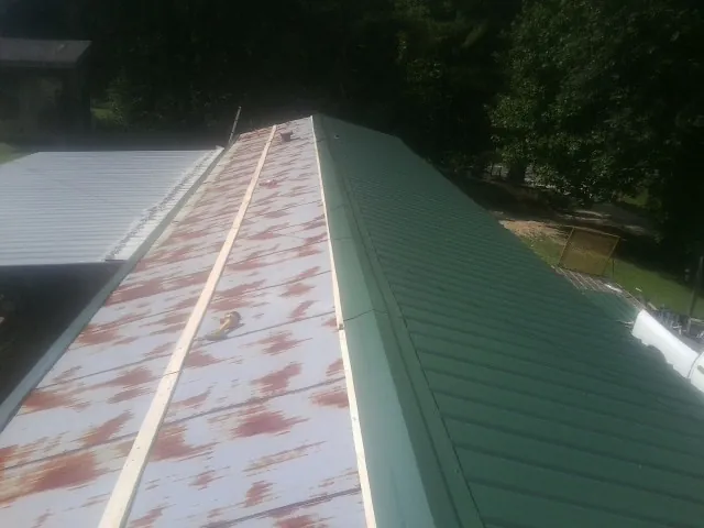 Old rusted panels beside newly installed green metal roofing — Wind Damage Roof Repair by Roofing Brothers in Rio