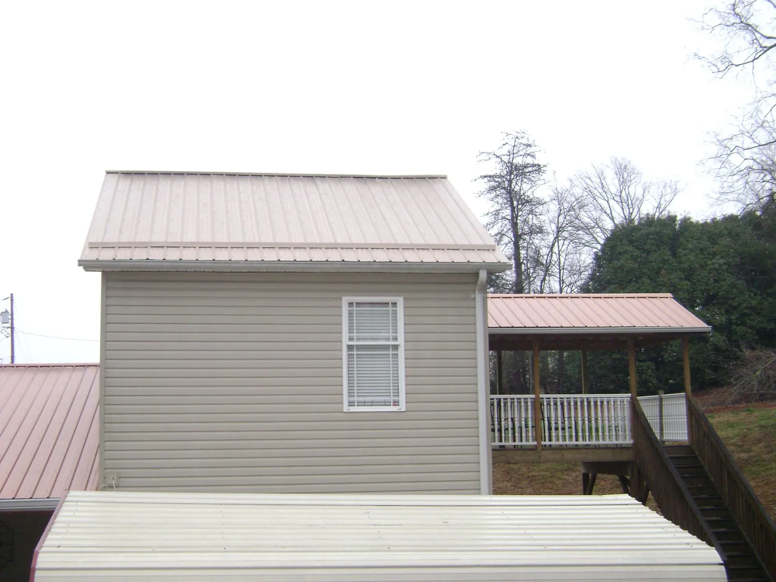 Tan metal roofs on a two story addition and attached porch, from a Roof Replacement job in Rio